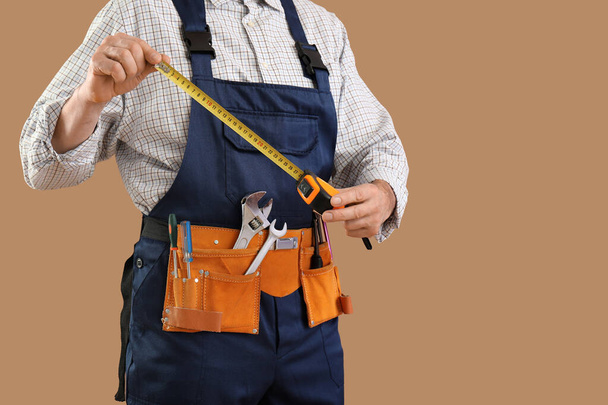 Чоловік будівельник з вимірювальною стрічкою та інструментами на коричневому фоні - Фото, зображення