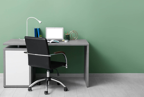 Moderno lugar de trabajo de oficina con portátil y sillón cerca de la pared verde - Foto, imagen