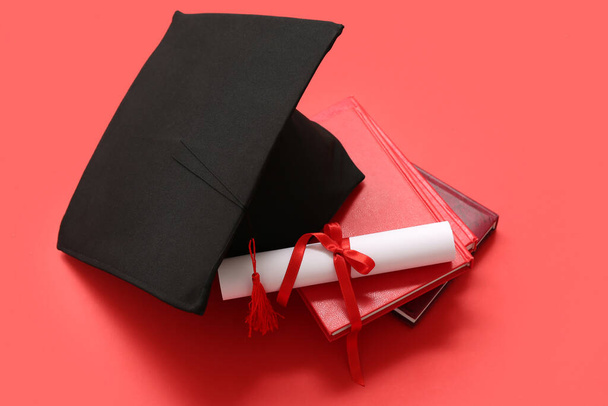 Cappello di laurea con diploma e taccuini su sfondo rosso - Foto, immagini
