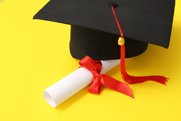 Graduation hat and diploma on yellow background - Photo, Image