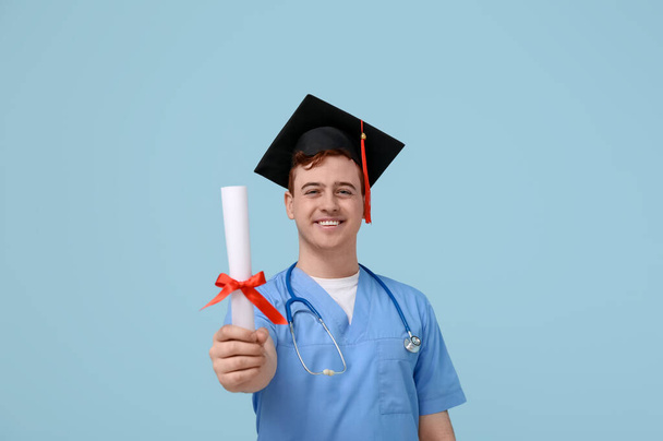 Estudante masculino em placa de argamassa e uniforme de médico com diploma em fundo azul - Foto, Imagem