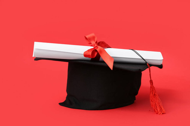Mortierbord en diploma op rode achtergrond - Foto, afbeelding