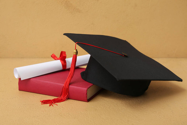 Mortar board with diploma and book on brown background - Photo, Image