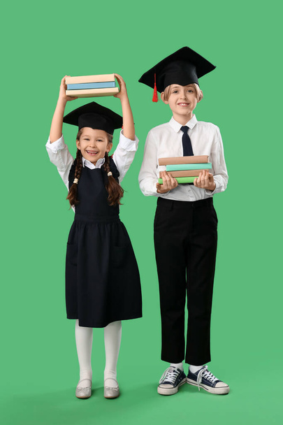 Kleine Kinder in Abschlussmützen mit Büchern auf grünem Hintergrund. Ende des Schuljahres - Foto, Bild