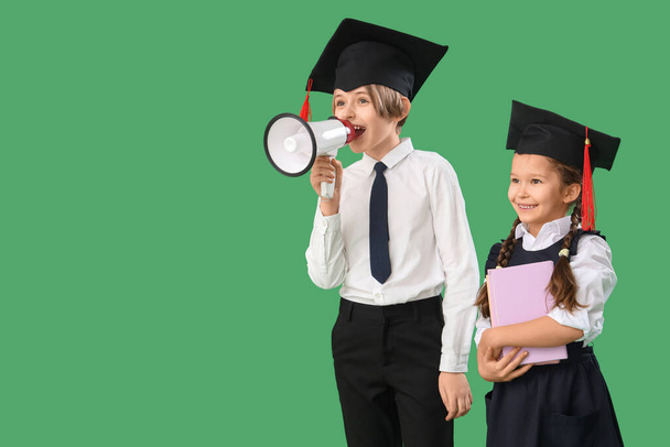 Małe dzieci w kapeluszach dyplomowych z książkami krzyczącymi do megafonu na zielonym tle. Koniec roku szkolnego - Zdjęcie, obraz