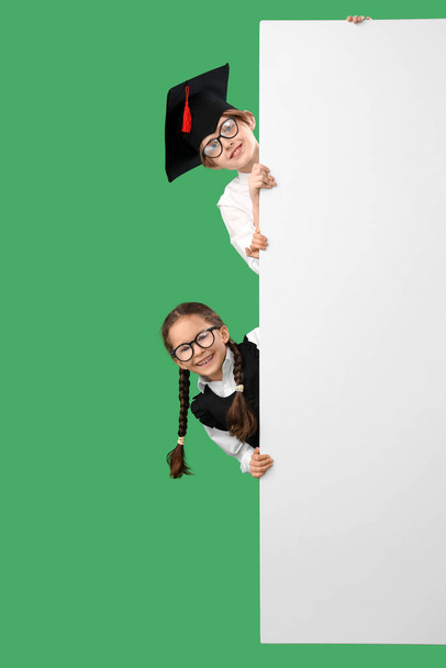 Little children in graduation hats with blank poster on green background. End of school year - Photo, Image