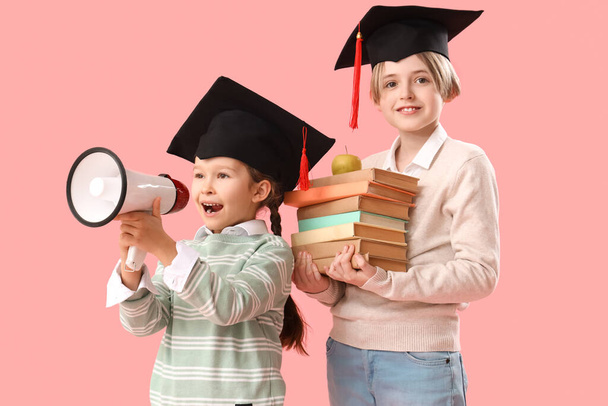 Niños pequeños con sombreros de graduación con libros y megáfono sobre fondo rosa. Fin del año escolar - Foto, imagen