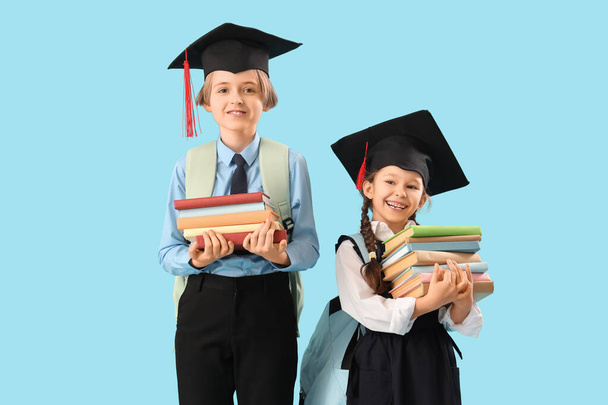 Kleine Kinder in Abschlussmützen mit Büchern auf blauem Hintergrund. Ende des Schuljahres - Foto, Bild