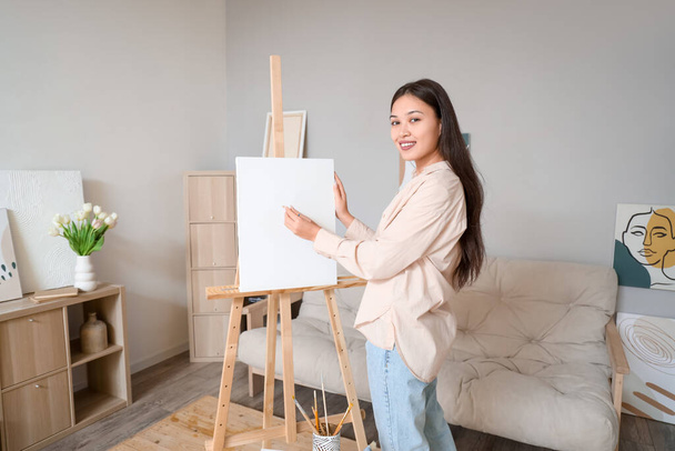 Female Asian artist drawing on easel at home - Photo, Image