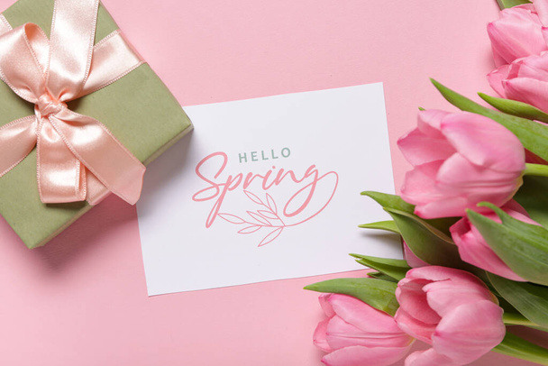 Biglietto di auguri con testo HELLO PRIMAVERA, confezione regalo e bellissimi tulipani su sfondo rosa - Foto, immagini
