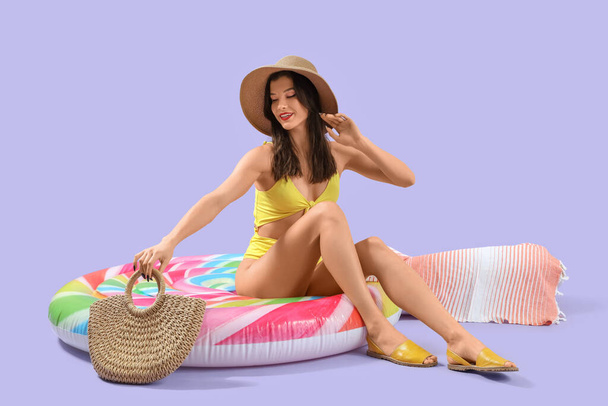 mooie jonge vrouw in strand slijtage op zwemmen ring tegen lila achtergrond - Foto, afbeelding