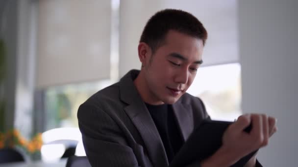 Joven empresario asiático escribiendo datos de trabajo en su tableta en el escritorio. Imágenes de alta calidad 4k - Imágenes, Vídeo