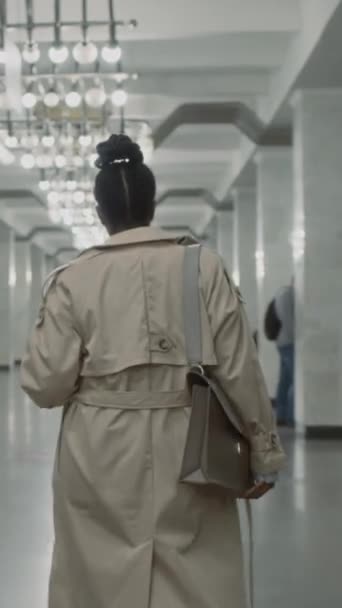 Lentitud de seguimiento vertical de señora anónima en gabardina y con bolsa de cuero caminando por el paso subterráneo iluminado vacío del metro - Imágenes, Vídeo