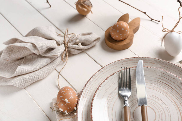 Nastavení stolu pro velikonoční oslavu s látkou a malovanými vejci na bílém dřevěném pozadí - Fotografie, Obrázek