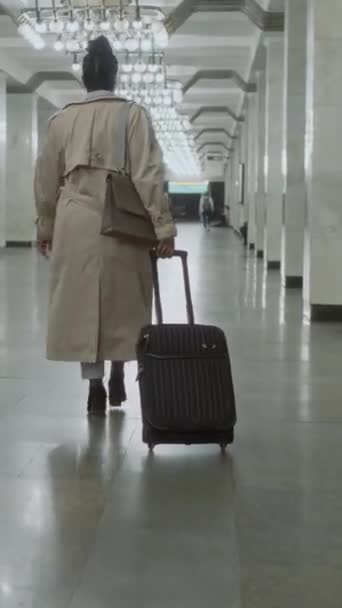 Tylne pionowe nagranie niezidentyfikowanej kobiety w płaszczu, spacerującej wzdłuż długiej peronu metra z bagażem podczas podróży - Materiał filmowy, wideo