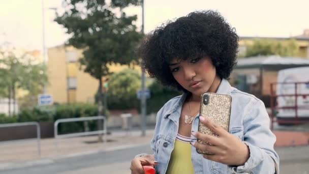 Slow motion video van een transgender vrouw het nemen van een selfie in de straat, terwijl het houden van oranje koptelefoon - Video