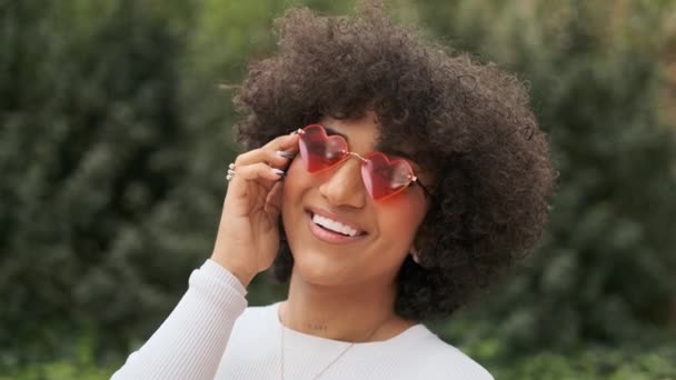 Vídeo en cámara lenta de una mujer trans feliz posando juguetonamente con gafas de sol en forma de corazón - Metraje, vídeo