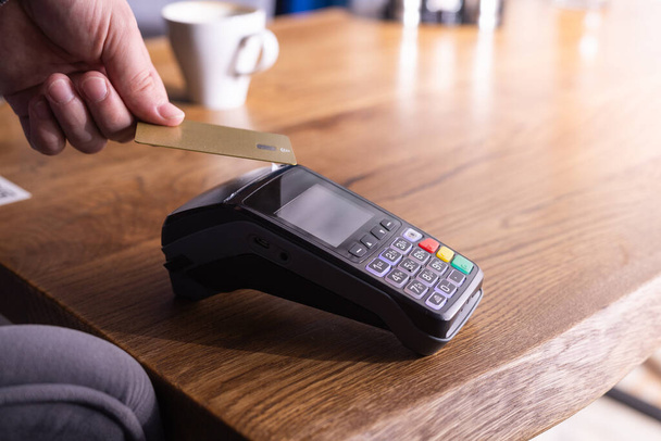 NFC hitelkártyás fizetés. Nő fizet érintésmentes hitelkártyával NFC technológiával. Vezeték nélküli pénz tranzakció. Kártyagép férfi kezében napfény háttér - Fotó, kép