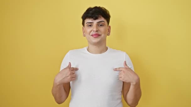 Opgewonden jongeman in vreugde, met een zelfverzekerde glimlach en met optimisme wijzend op een gele, geïsoleerde achtergrond, met een wit t-shirt aan - Video