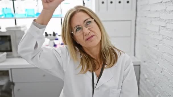 Die freche blonde Wissenschaftlerin mittleren Alters, die im Labor sitzt, macht sich über Menschen mit "Verlierer" -Stirn-Geste lustig, lacht, neckt und beleidigt - Filmmaterial, Video