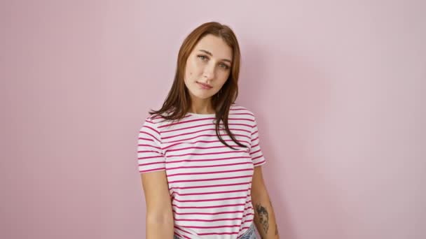 Cheery young brunette in stripes offering help over pink background - Footage, Video