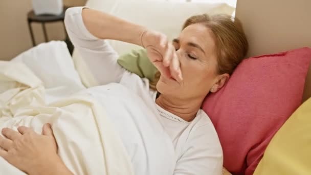 Dojrzała kobieta wydaje się chora, gdy spoczywa w sypialni, wyrażając dyskomfort leżąc w łóżku.. - Materiał filmowy, wideo