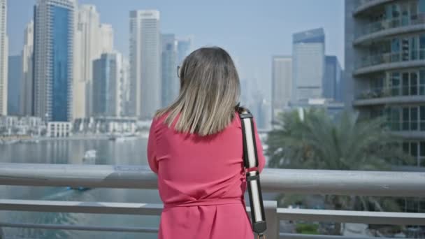 A smiling woman in a pink dress enjoys the view of the dubai marina skyline and waterfront on a sunny day. - Footage, Video