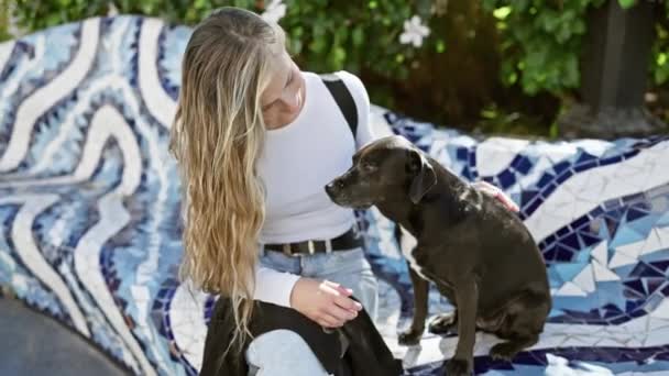 Szőke nő szeretettel háziállat fekete kutya a színes városi kertben. - Felvétel, videó