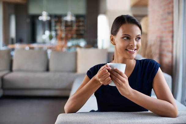 Ευτυχισμένη γυναίκα, σκέφτεται και πίνοντας καφέ στο σπίτι στον καναπέ για να χαλαρώσετε, την ειρήνη ή το σχεδιασμό στο πρωινό το πρωί. Όνειρο, φλιτζάνι τσάι και πρόσωπο με ιδέα για espresso, latte και χαμόγελο στο σαλόνι. - Φωτογραφία, εικόνα