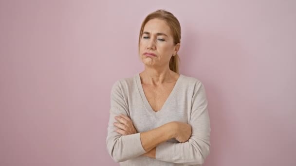 Cranky middle age blonde woman, a mature skeptic person with crossed arms, disapproving frown on face expresses serious doubt over pink isolated background. - Footage, Video