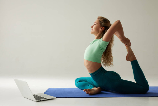 девушка делает утренние упражнения и растяжения онлайн на белом фоне, онлайн фитнес-тренировки - Фото, изображение