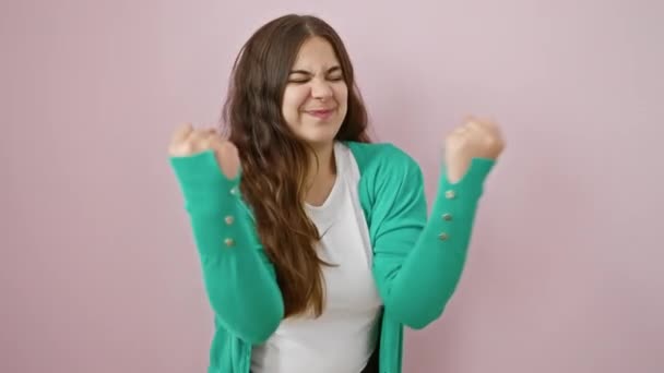 Iloinen nuori latino nainen juhlii voittoa voittajan ele, innoissaan hymy, menestyksen huuto ja hauskaa vaaleanpunainen eristetty tausta - Materiaali, video