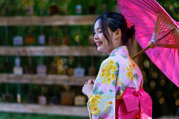 Une jeune femme portant un kimono traditionnel japonais ou un yukata tenant un parapluie est heureuse et joyeuse dans le parc. Robe d'été traditionnelle japonaise. - Photo, image