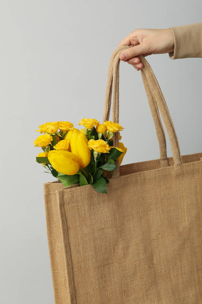 Bolso con flores en mano femenina sobre fondo gris - Foto, Imagen
