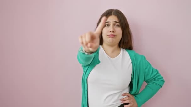 La joven y ardiente mujer hispana da una severa advertencia, señalando con el dedo hacia arriba en un gesto de no sobre el aislado fondo rosa, expresión gritando '¡Alto!' - Imágenes, Vídeo