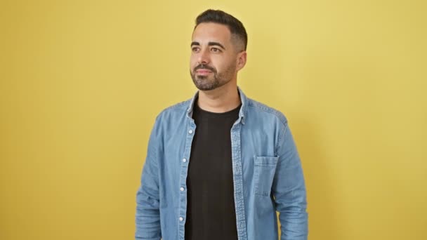 Fröhlicher hispanischer Typ im Jeanshemd, die Hand schützende Augen, weit hinaus suchend mit selbstbewusstem Lächeln vor gelbem Hintergrund - Filmmaterial, Video
