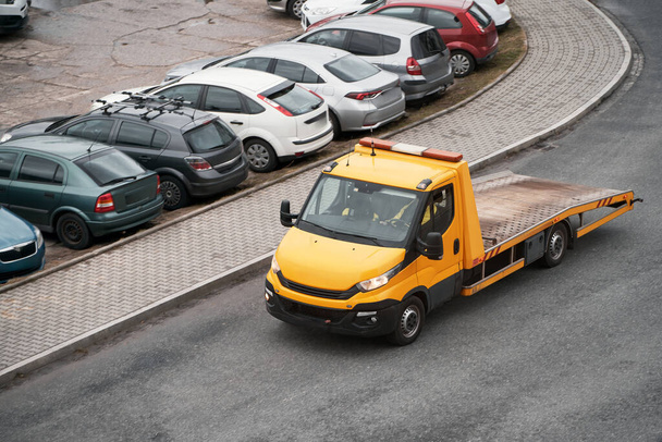 Um caminhão de reboque laranja com uma mesa e um guincho na frente está pronto para ajudar um carro quebrado em uma rua da cidade. - Foto, Imagem