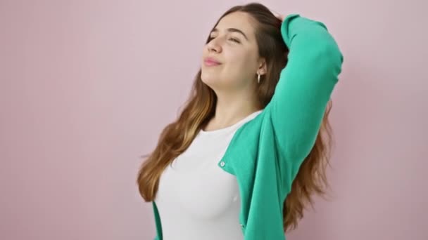 Magabiztos fiatal spanyol nő megérinti a haját, feltűnő divatos pózt; gyönyörű mosolya sugárzik öröm felett elszigetelt rózsaszín háttér - Felvétel, videó