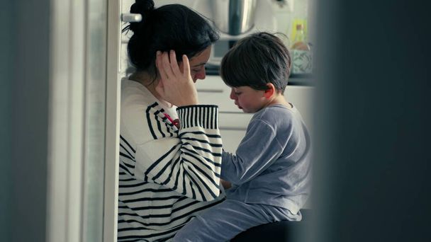 Открытая мать, объясняющая плохое поведение ребенка в заботливых теплых объятиях после травмы в нежной подлинной любящей сцене на кухне, родительское руководство - Фото, изображение