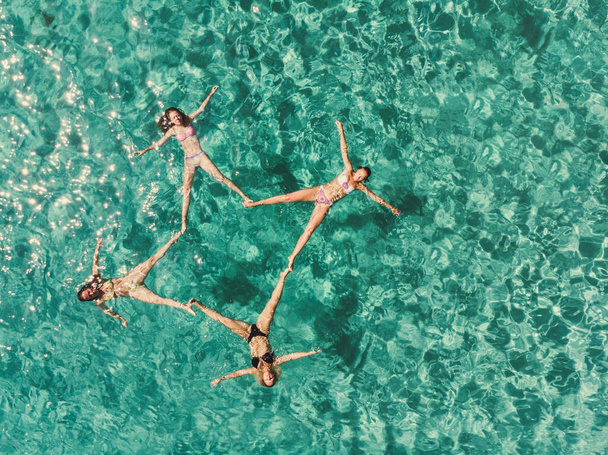 トロピカルターコイズの水に浮かびながらリラックスした4人の美しい女性の友人の空中撮影. - 写真・画像