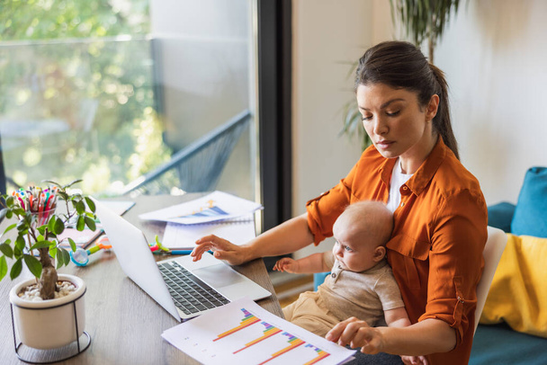 Žena podnikatel pracuje na notebooku a starat se o své dítě doma. - Fotografie, Obrázek