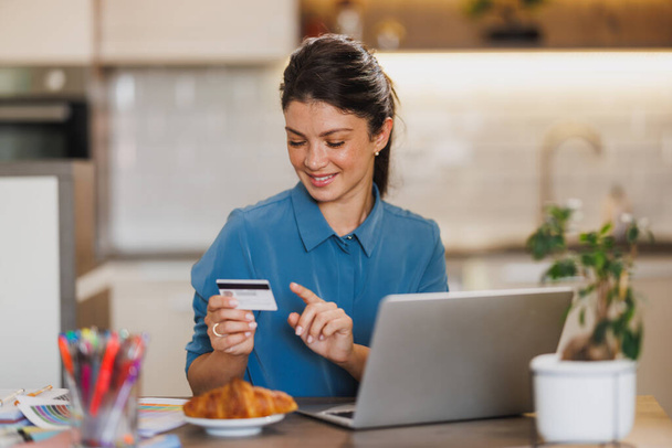 Młoda kobieta przedsiębiorca przy użyciu karty kredytowej do dokonywania płatności online na laptopie w domu. - Zdjęcie, obraz