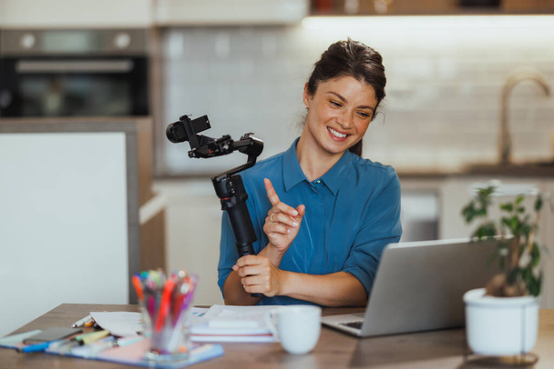 Mujer vlogging sobre productos de fotografía y mostrando gimbal para la cámara mientras hace una videollamada en su computadora portátil en casa. - Foto, imagen