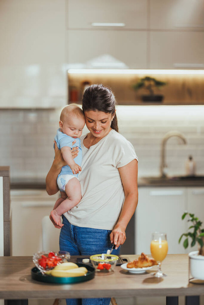 Multitâche mère tenant son bébé alors qu'elle fait un repas sain à la maison. - Photo, image