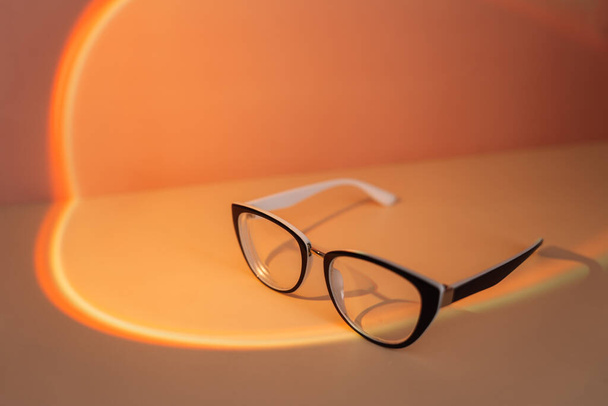 Óculos de visão com molduras pretas sob luz laranja. - Foto, Imagem