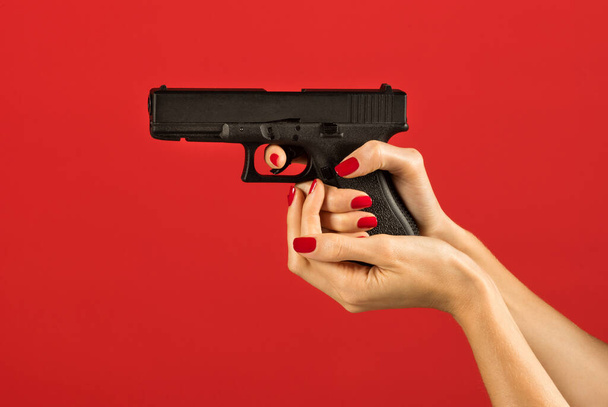 Неузнаваемая стройная женщина держит пистолет в правой руке, держа указательный палец с лаком для ногтей на спусковом крючке и поддерживая камеру магазина ладонью - Фото, изображение