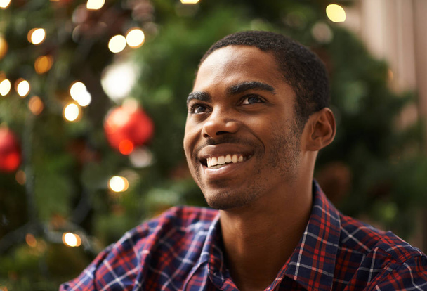 Άνθρωπος, σκέψη και ευτυχισμένη στο σπίτι τα Χριστούγεννα για γιορτή, διακοπές και εορταστική πνεύμα στο σαλόνι. Αφρικανός, στοχαστικός και χαμογελαστός τα Χριστούγεννα με χαλάρωση, αυτοπεποίθηση και διακοπές στο διαμέρισμα. - Φωτογραφία, εικόνα