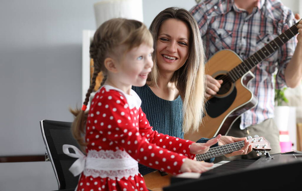 A szülők gitároznak, a lányuk szintetizátor. Zenélés közben a gyermek matematikai képességeket fejleszt. A gyerek megtanulja megérteni a zenét. A szülők figyelemmel kísérik a gyerekek testtartását az óra alatt - Fotó, kép