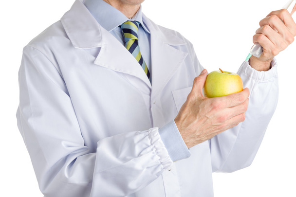 man in medical white coat makes an injection to yellow apple - Foto, imagen