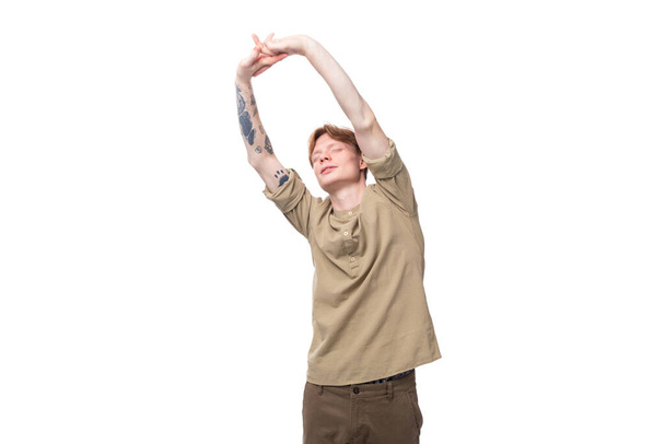 a young European guy with red hair is dressed in a fashionable beige shirt and brown trousers doing exercises. - 写真・画像